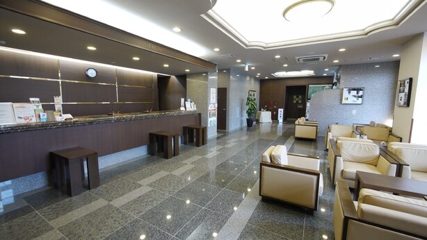 Una hall d'albergo con reception, area salotto e orologio a parete.
