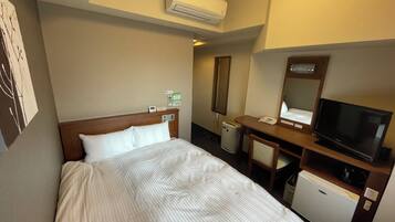 A hotel room with a bed, a desk with a chair, a television, a mini-fridge, and an air conditioning unit.