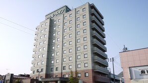 Un hôtel à plusieurs étages doté d’une architecture moderne, avec une entrée imposante, un espace abrité et une signalétique indiquant les différents services proposés.