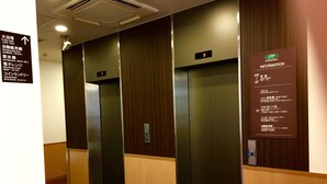 Un hall d’hôtel avec trois ascenseurs, un panneau d’affichage contenant des informations et un plancher en bois.