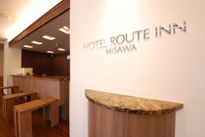 Un mostrador de recepción con un cartel que dice "HOTEL ROUTE INN MISAWA" y bancos de madera al fondo.