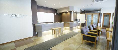 A hotel reception area with a counter, seating area, and a visible clock.