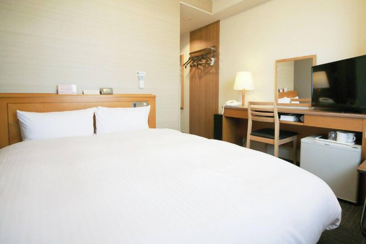 Hotellihuone, jossa on suuri sänky, työpöytä tuolilla, televisio ja pieni jääkaappi.