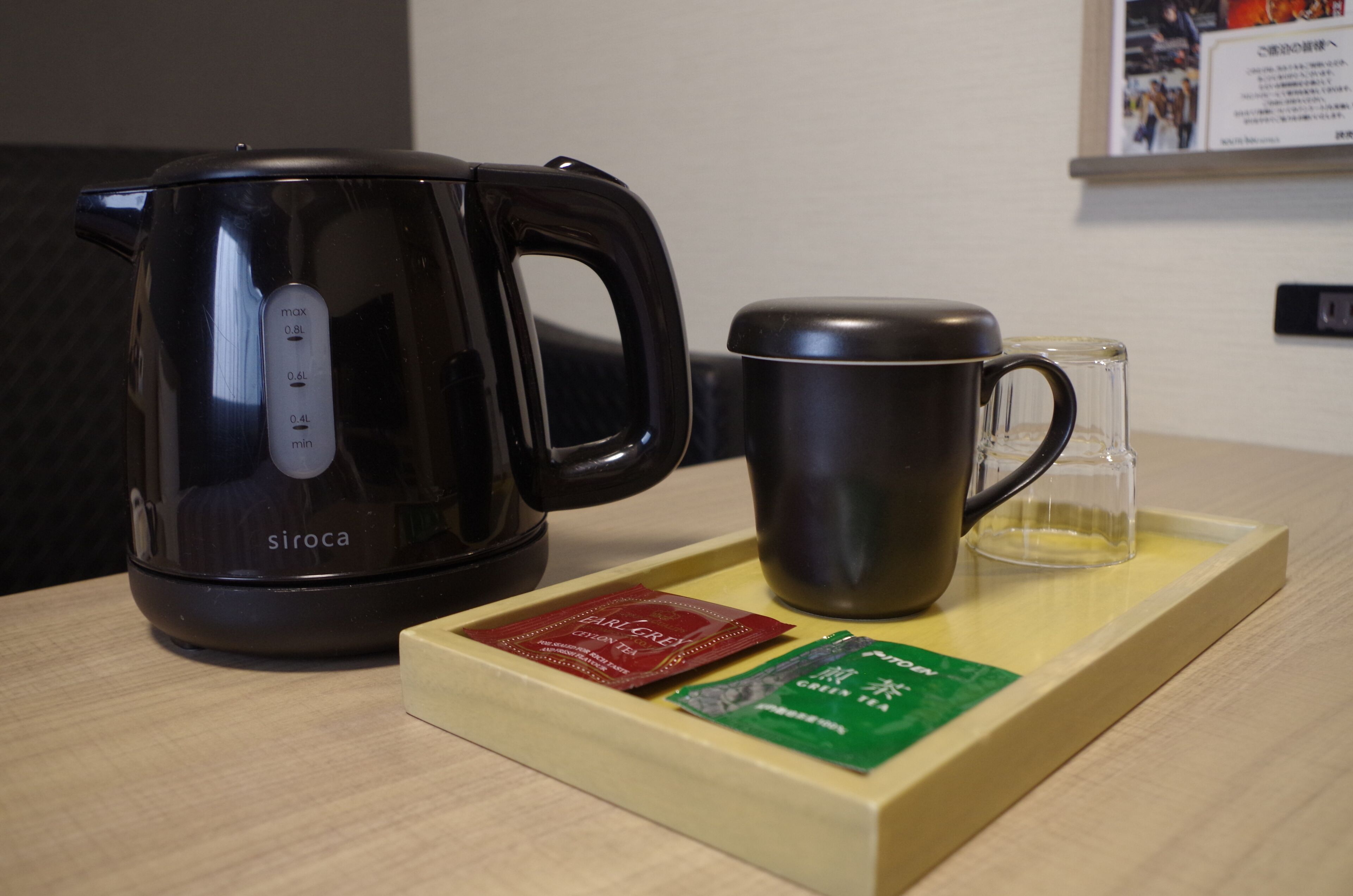 A black electric kettle, a dark mug, and a tray with two packets of tea on a wooden table.