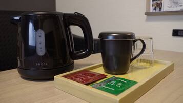 A black electric kettle, a dark mug, and a tray with two packets of tea on a wooden table.