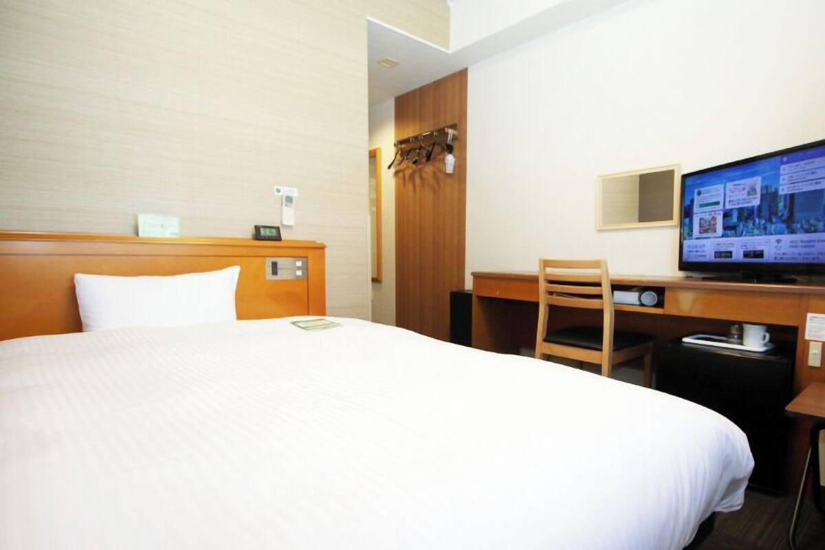 Hotellihuone, jossa on suuri sänky, työpöytä tuolilla, televisio ja pieni kahvinkeitin.