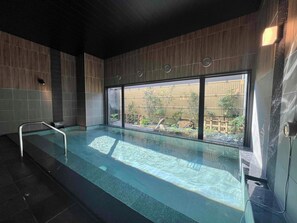 Una piscina con una escalera metálica, paredes de paneles de madera y grandes ventanales con vistas a un jardín de bambú.