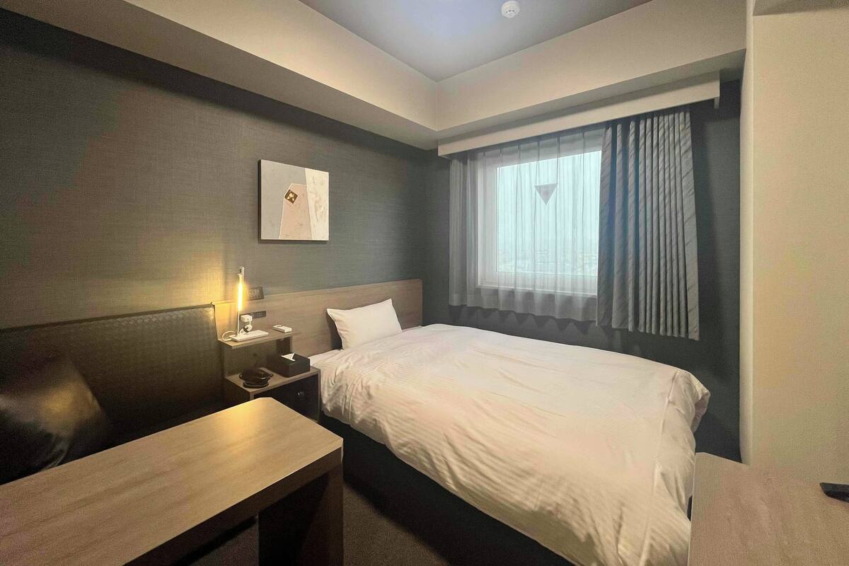 A hotel room with a bed, bedside table, lamp, and a window with curtains.