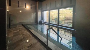A modern indoor swimming pool with a glass barrier, tiled floor, and a view of a bamboo fence outside.