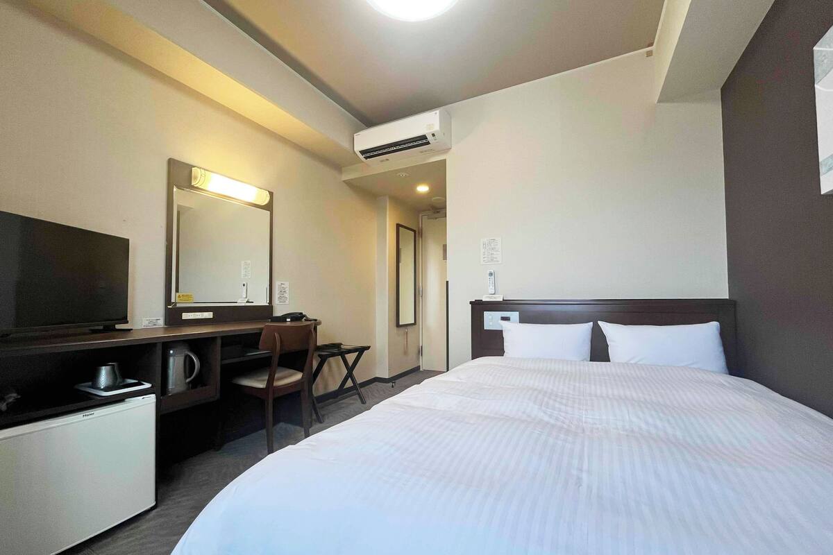 A hotel room with a bed, a desk with a chair, a television, a coffee maker, and a mirror.
