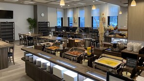 A modern breakfast buffet with multiple food stations, a clock, and a TV on the wall.