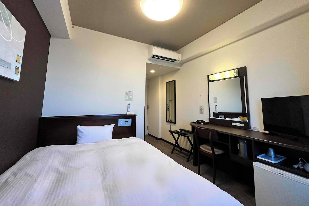 A hotel room with a bed, a desk, a chair, a television, and an air conditioning unit.