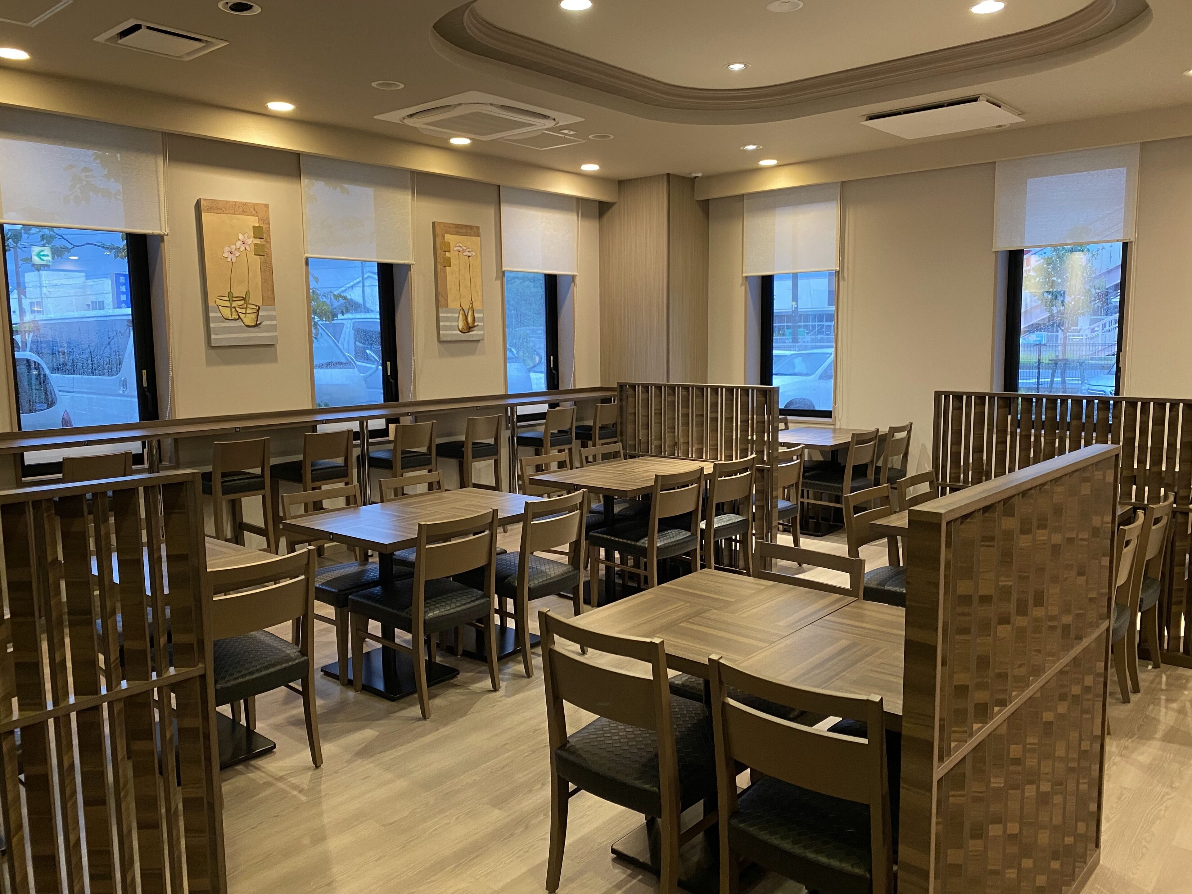 A restaurant with wooden tables and chairs, large windows, and artwork on the walls.