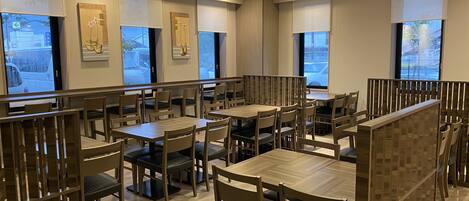 A restaurant with wooden tables and chairs, large windows, and artwork on the walls.