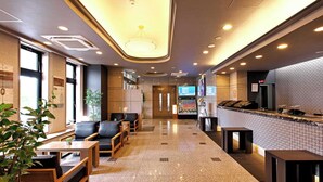 A hotel lobby with seating areas, a reception desk, and a large screen displaying information.