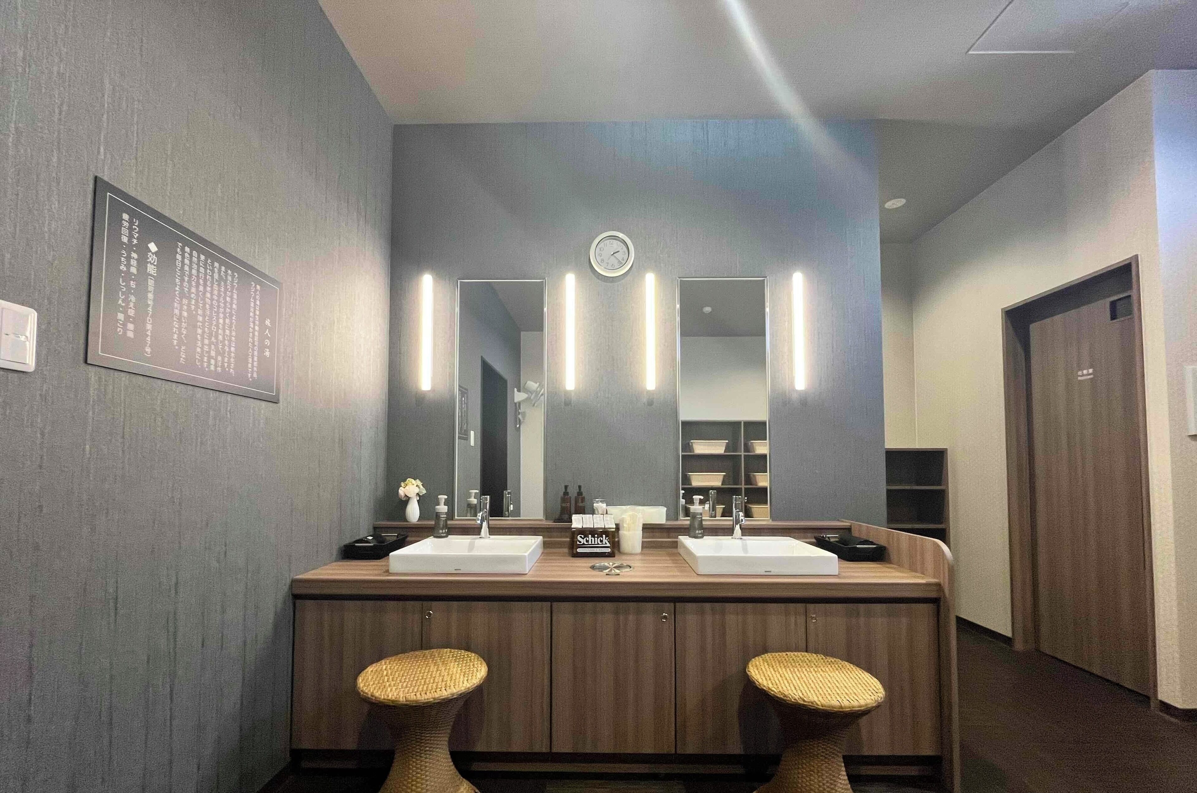 A modern bathroom with two sinks, a large mirror, and a clock on the wall.