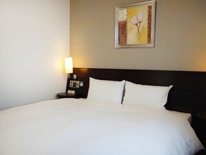 A neatly made bed with white linens, a bedside table with a lamp, and a framed picture on the wall.