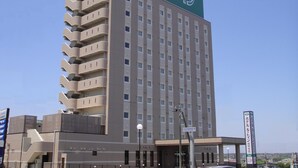 A multi-story hotel with a green and beige facade, multiple balconies, and a clear sky in the background.