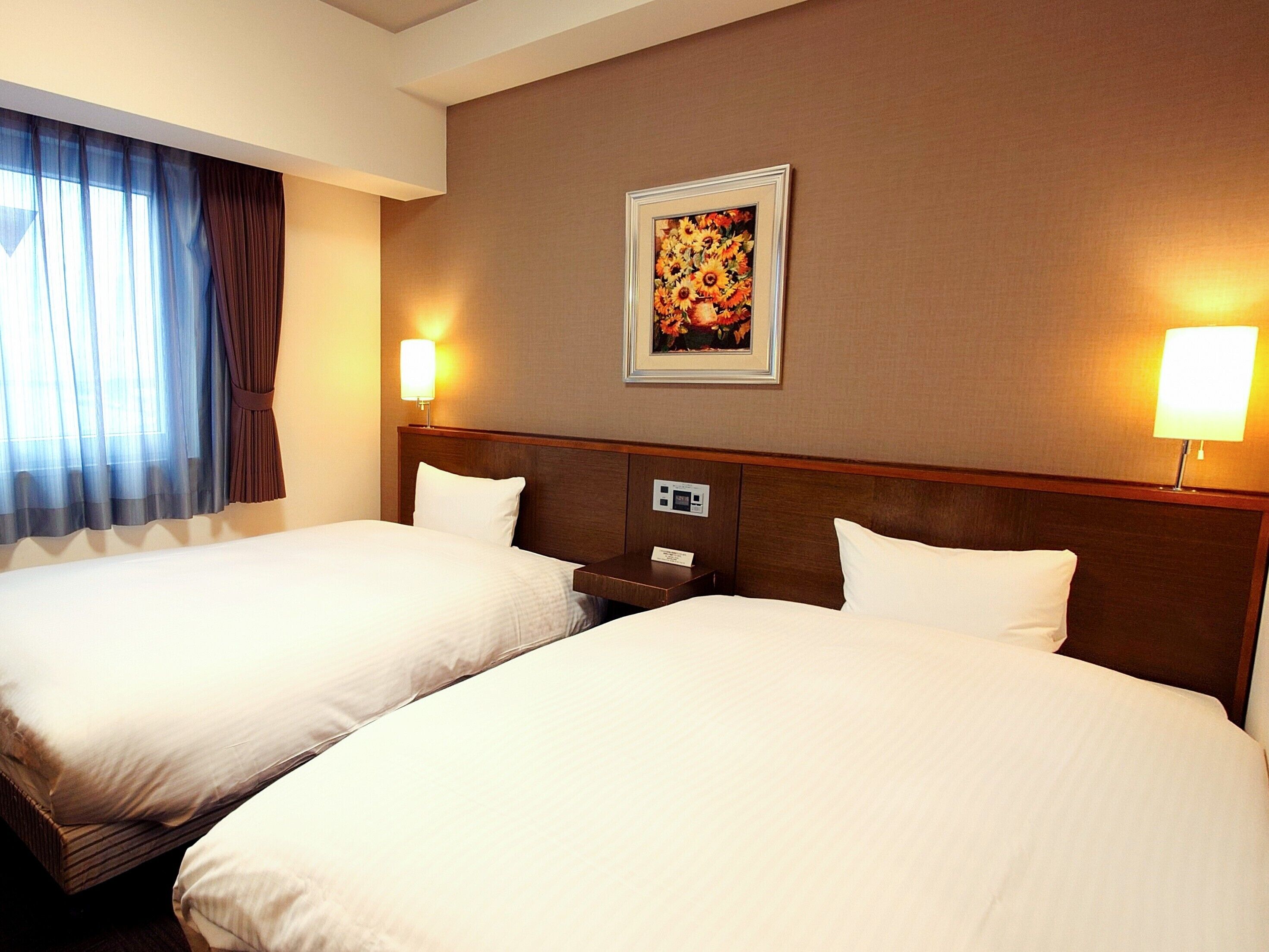 A hotel room with two beds, a nightstand, a painting on the wall, and two wall lamps.