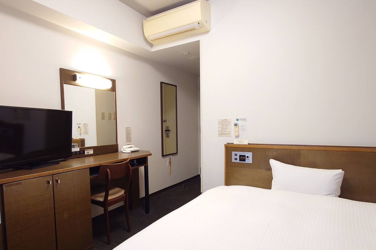 A hotel room with a bed, a desk with a television, a chair, and a mirror.
