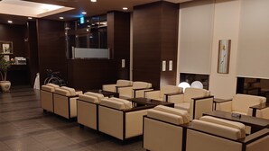 A modern lounge area with multiple seating options, a reception desk, and a television screen. - Hotel Route - Inn Yurihonjyo (Yurihonjo)