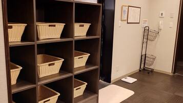 A room with a wooden floor, a dark wooden shelving unit with wicker baskets, a white scale, and a metal cart.