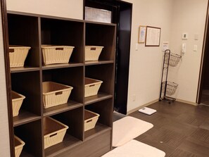 A room with a wooden floor, a dark wooden shelving unit with wicker baskets, a white scale, and a metal cart. - Hotel Route - Inn Yurihonjyo (Yurihonjo)