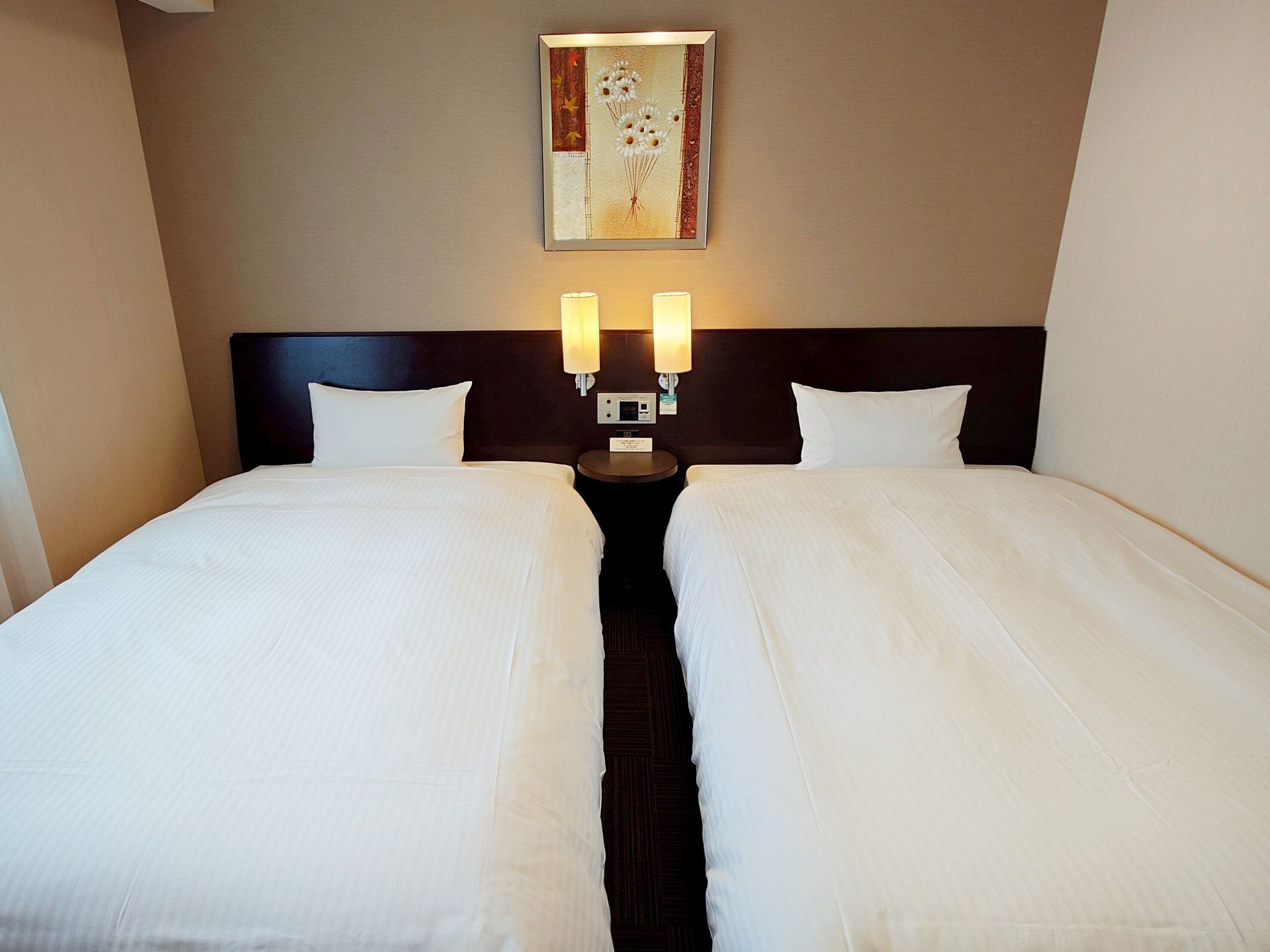 A double bed with two bedside tables, each with a lamp, in a hotel room.