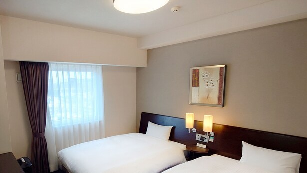 A hotel room with two beds, a desk, and a window with curtains.