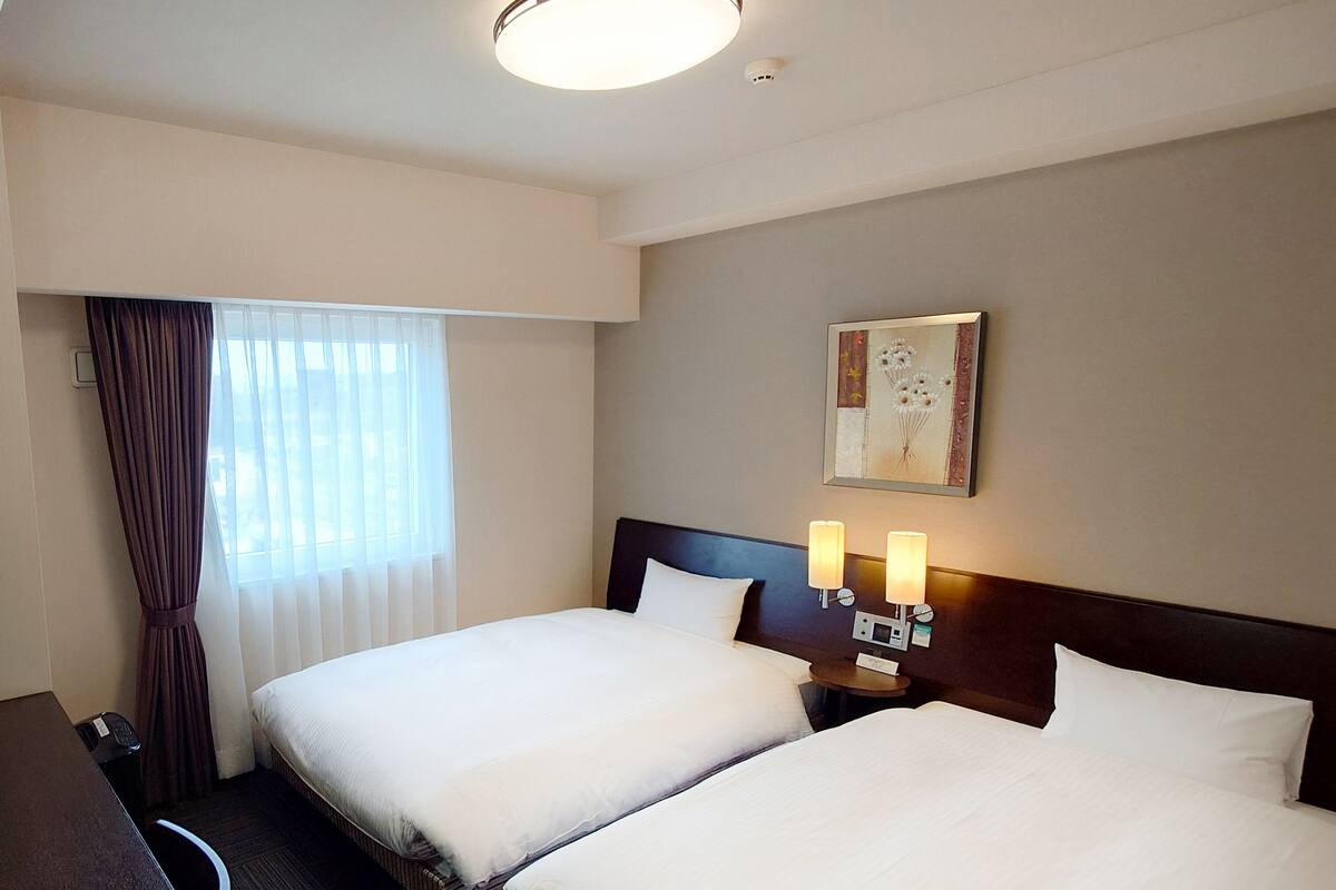 A hotel room with two beds, a desk, and a window with curtains.