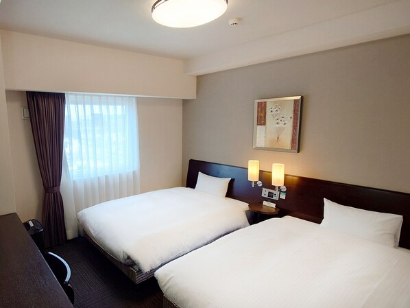 A hotel room with two beds, a desk, and a window with curtains.