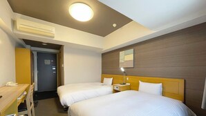 Une chambre d’hôtel avec deux lits, un bureau, une chaise, un appareil de climatisation et une table de chevet avec une lampe.
