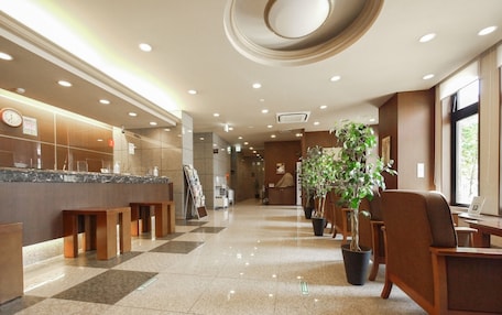 A hotel lobby with a reception desk, seating area, and potted plants.