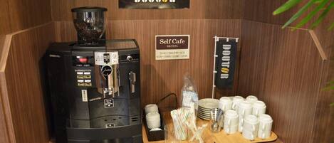 A self-service coffee station with a coffee machine, cups, and a sign indicating operating hours.