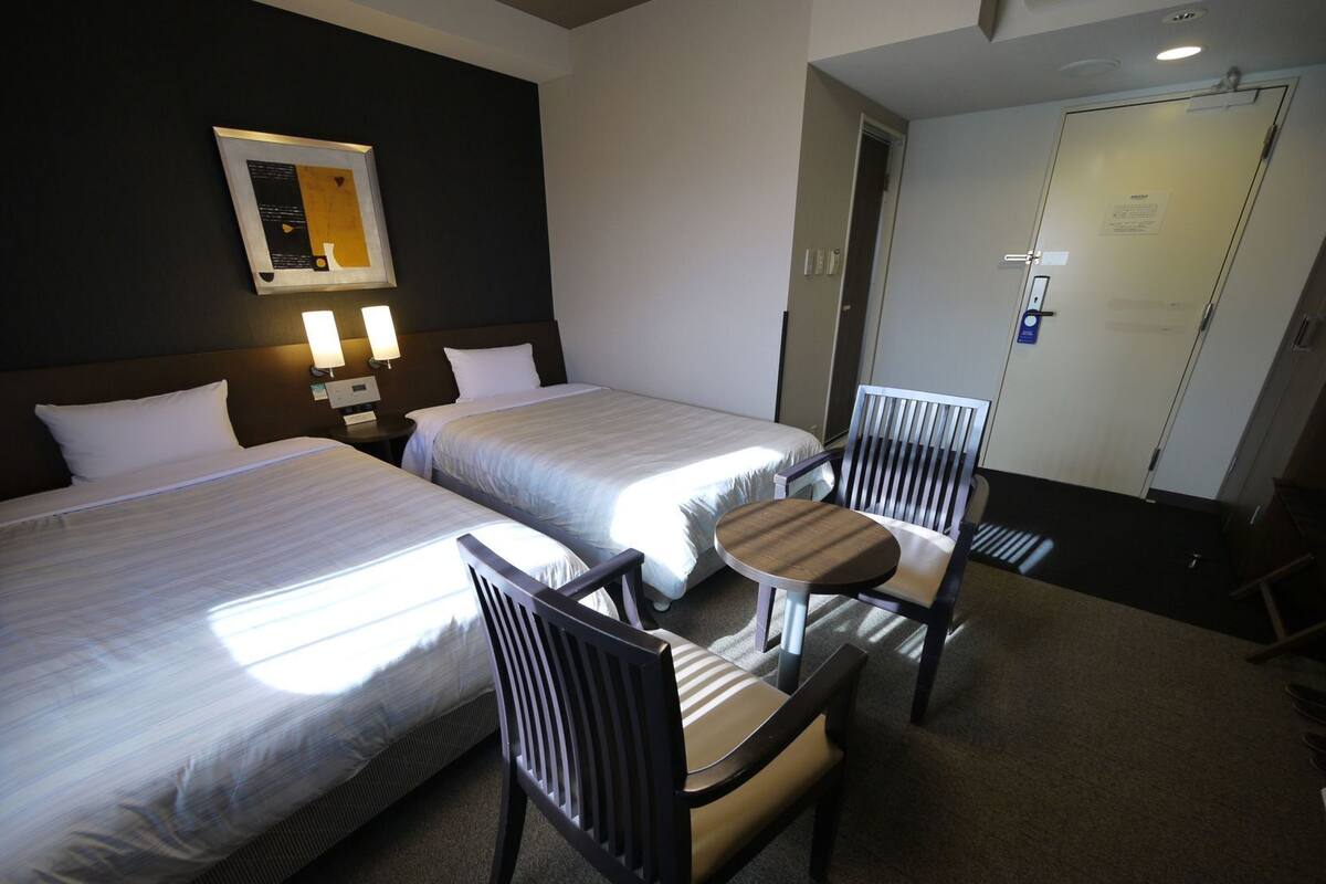 A hotel room with two beds, a small table, two chairs, and a wall-mounted artwork.