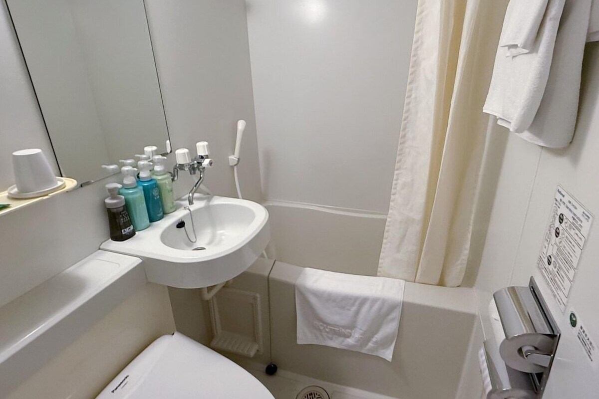 A bathroom with a sink, mirror, toiletries, and a towel rack.
