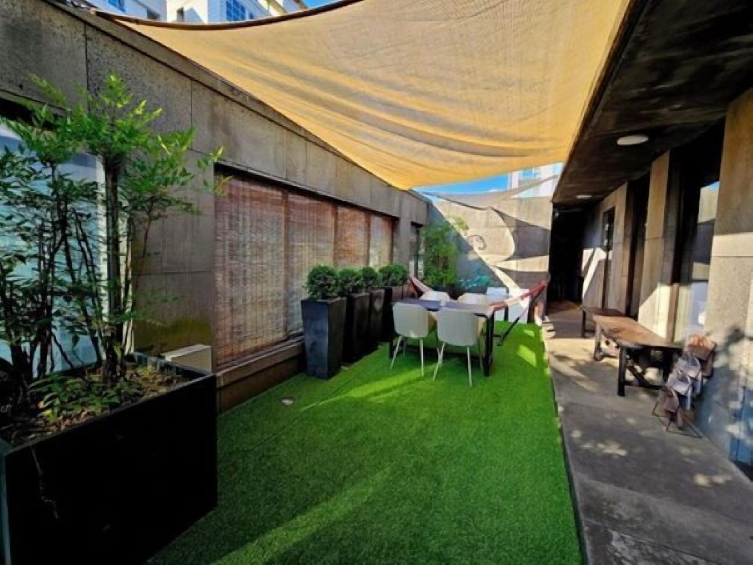Un patio exterior moderno con césped artificial, una mesa y sillas, y un toldo amarillo.