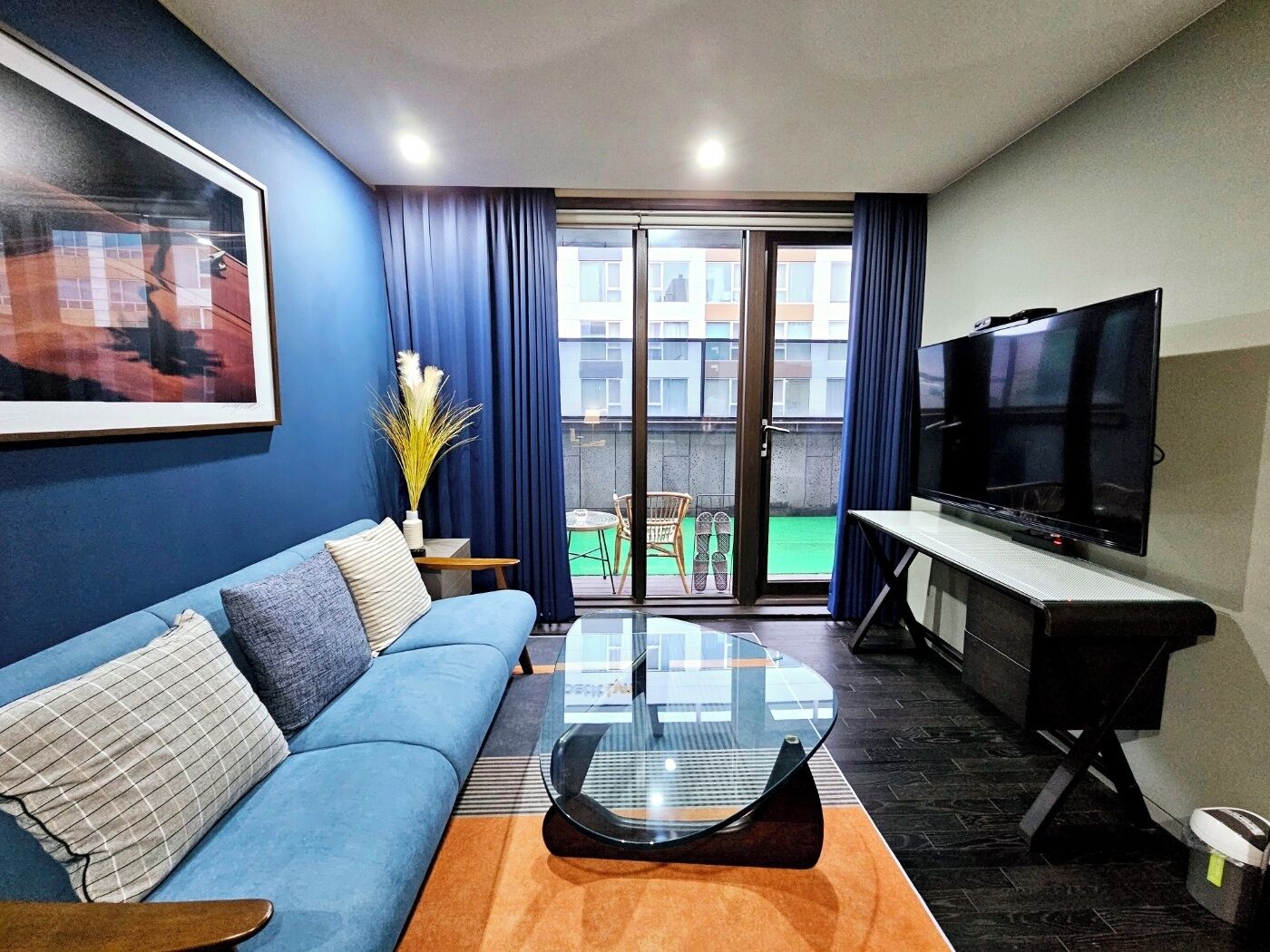 A modern living room with a blue sofa, a glass coffee table, and a flat-screen TV.