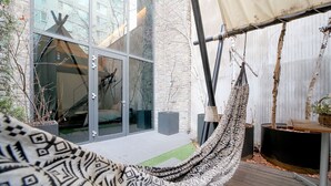 Un espacio exterior moderno con puerta de cristal, una hamaca y una terraza de madera.