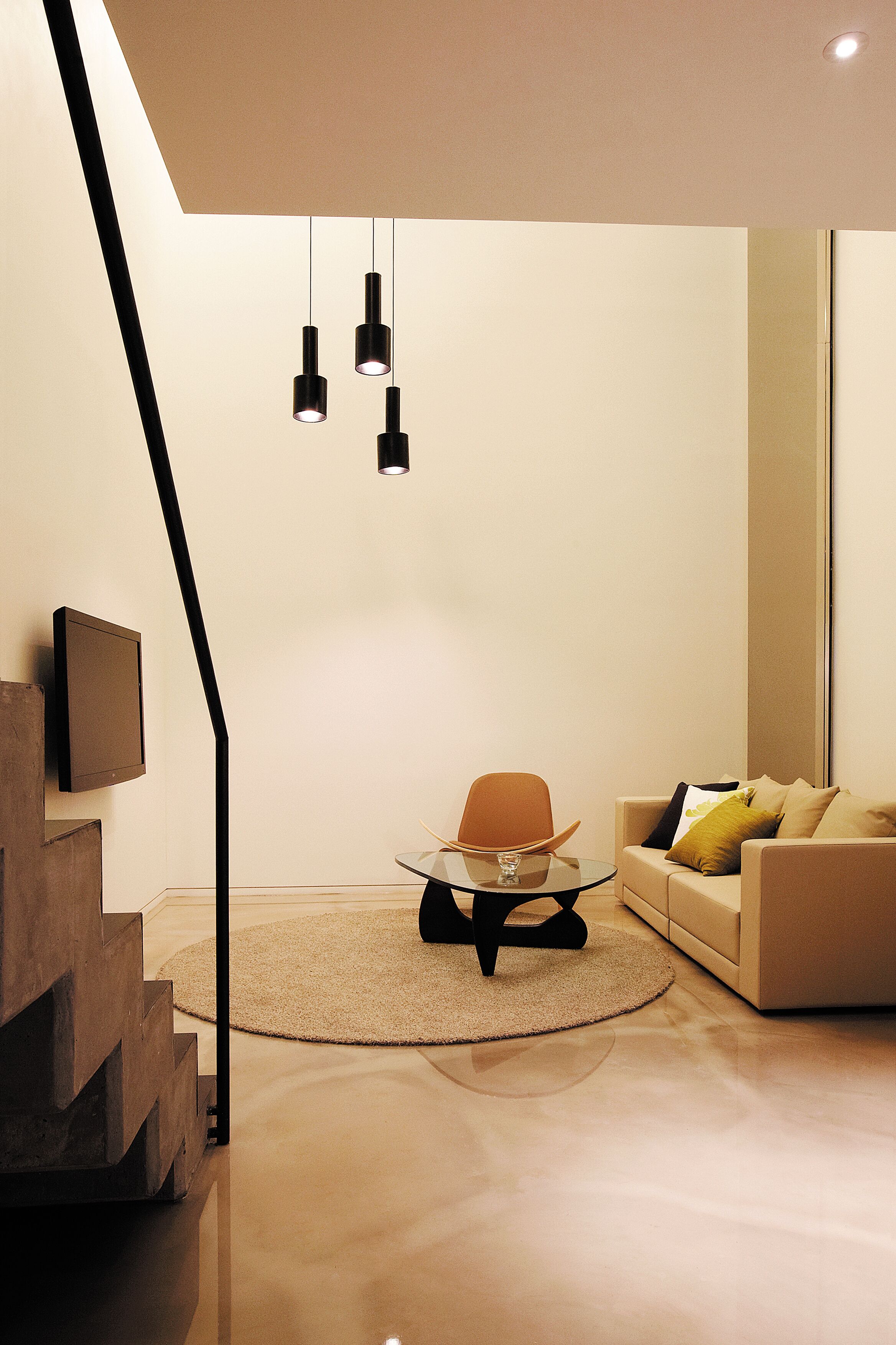 Uma sala de estar moderna com um sofá, uma mesa de centro e uma poltrona. Escada com design diferenciado à esquerda.
