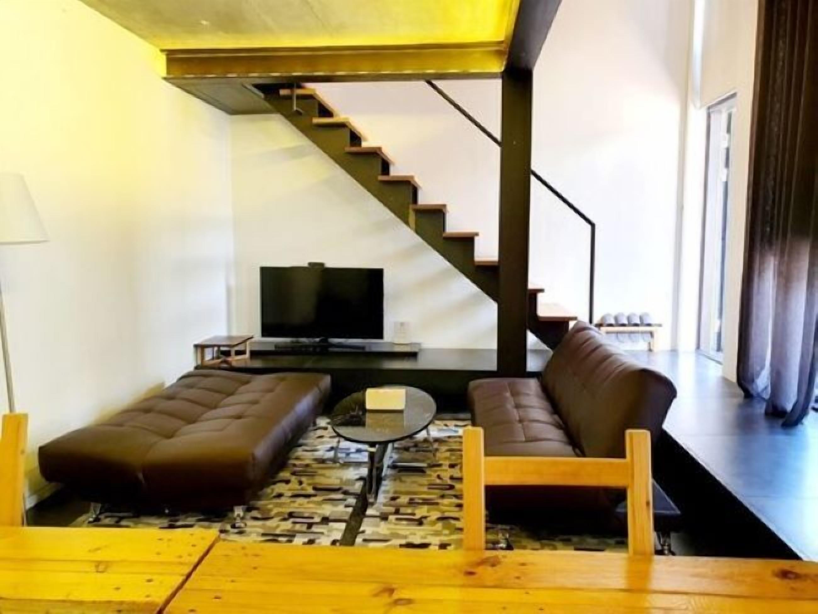 A modern living room with a sofa, a coffee table, and a TV. A staircase leads to a balcony.
