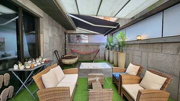 Un espace patio aménagé avec des meubles en osier, un hamac et une petite table dont le plateau est blanc.