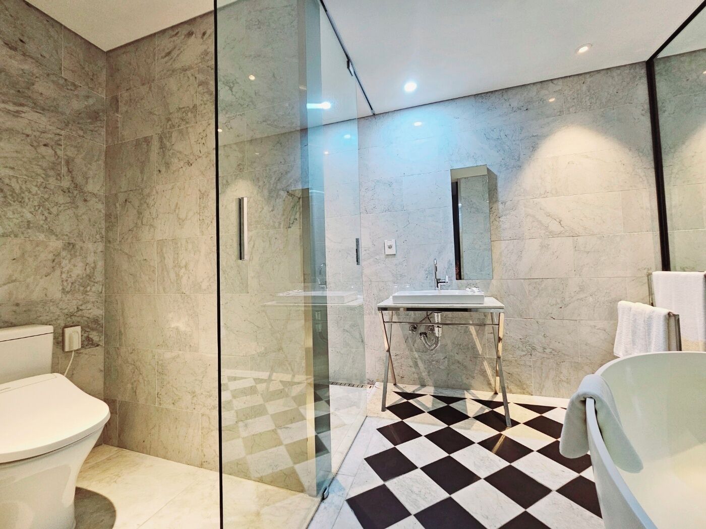Een moderne badkamer met een douchecabine van glas, een witte wastafel en een zwart-wit betegelde vloer.