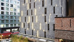 Un hotel moderno con fachada gris, múltiples ventanas y líneas verticales iluminadas.