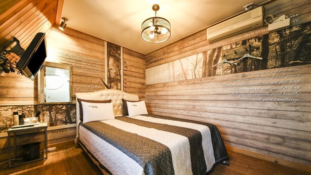 A cozy bedroom with a large bed, wooden walls, and a chandelier. - Q Hotel (Yongin)