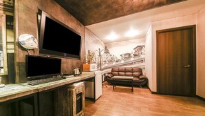 A cozy room with a wooden desk, a flat-screen TV, a leather sofa, and a mural of a cityscape. - Q Hotel (Yongin)