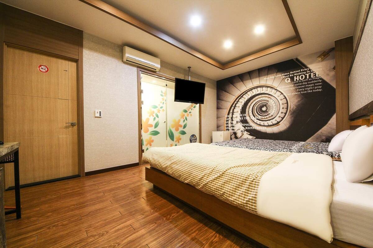 A hotel room with a bed, a TV, an air conditioning unit, and a poster on the wall.