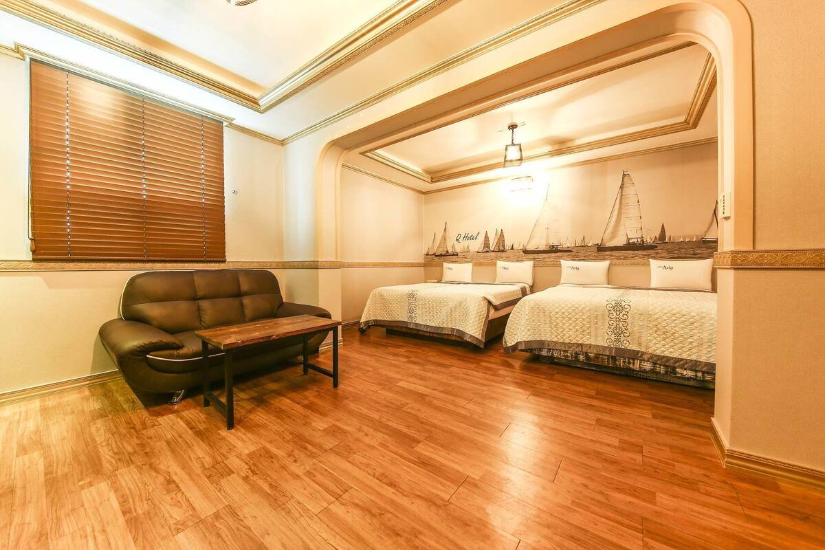 A hotel room with two beds, a leather armchair, a small table, and a wall mural of sailboats.
