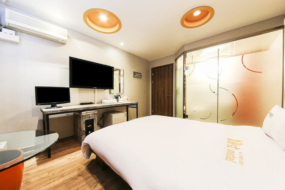 A hotel room with a bed, a desk with a computer, a TV, and a glass partition with circular designs.