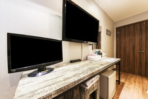 Una kitchenette con encimera de madera, dos monitores negros, un refrigerador pequeño y una puerta de madera.